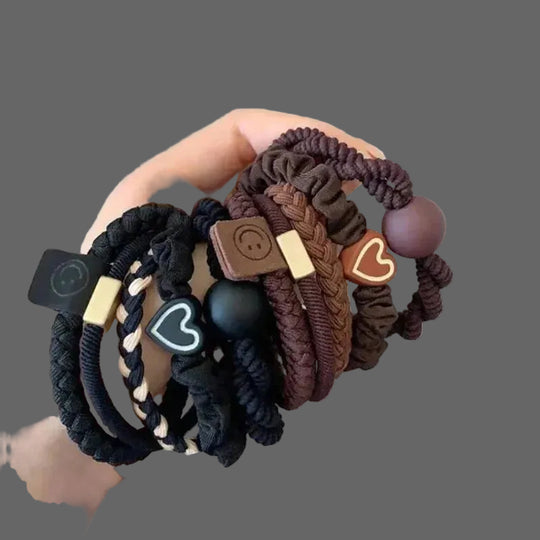 Hand holding a set of braided hair ties with decorative elements on a white background